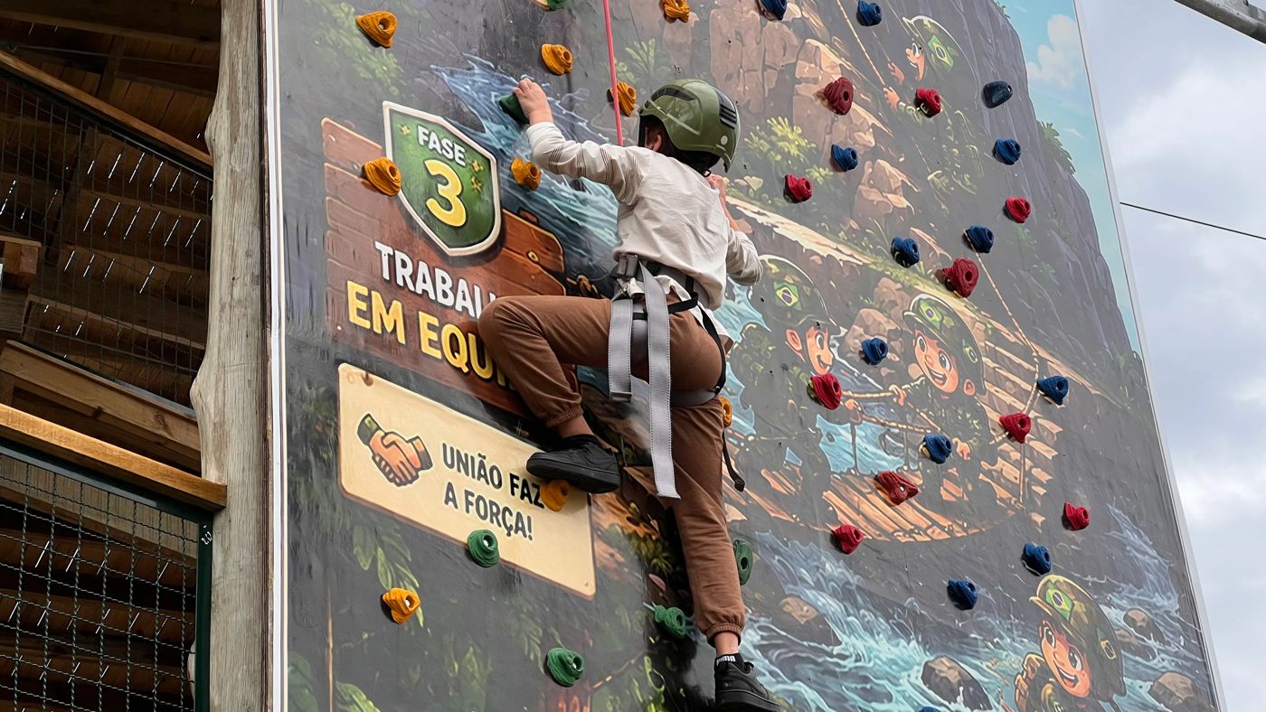 Criança escalando a parede de escalada com capacete e cadeirinha